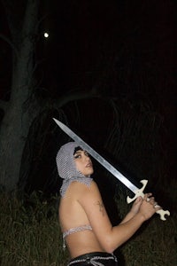 a woman holding a sword in front of a tree at night